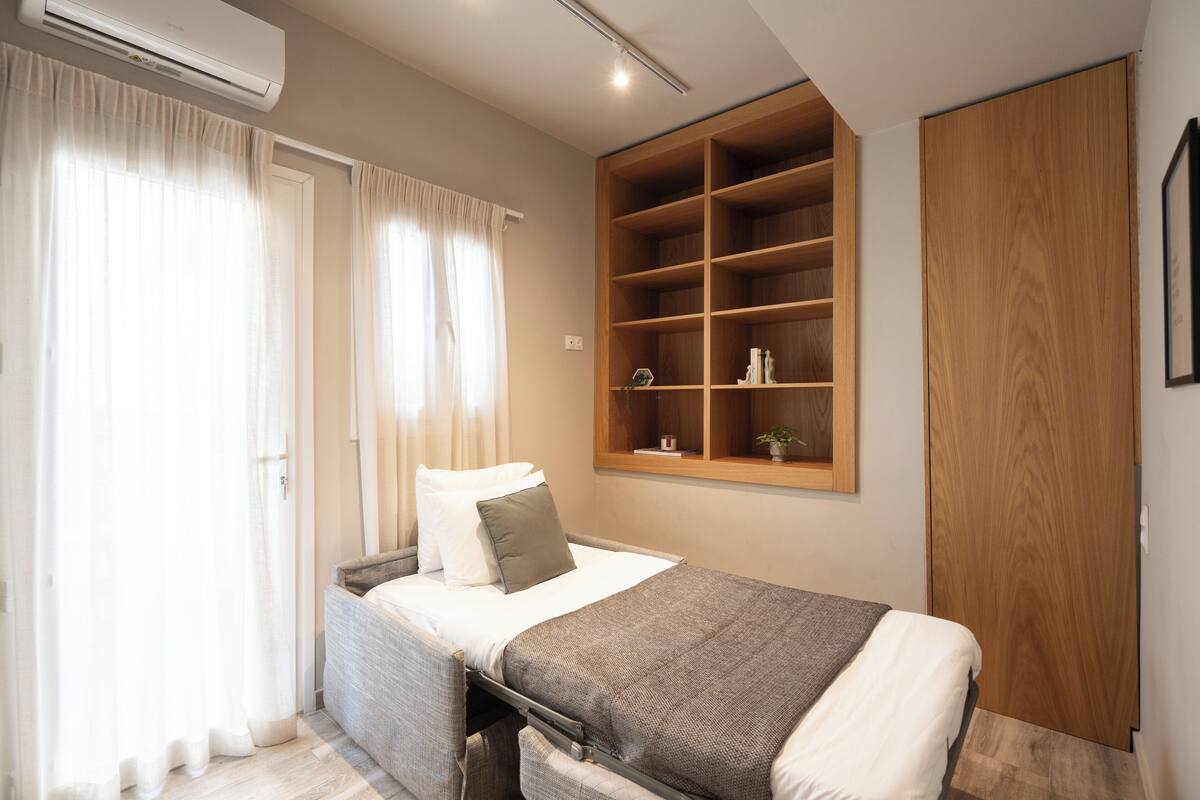 Ein Schlafzimmer mit einem Bett, einem Holzschrank, einer eingebauten Regaleinheit und einem Fenster mit Vorhängen.
