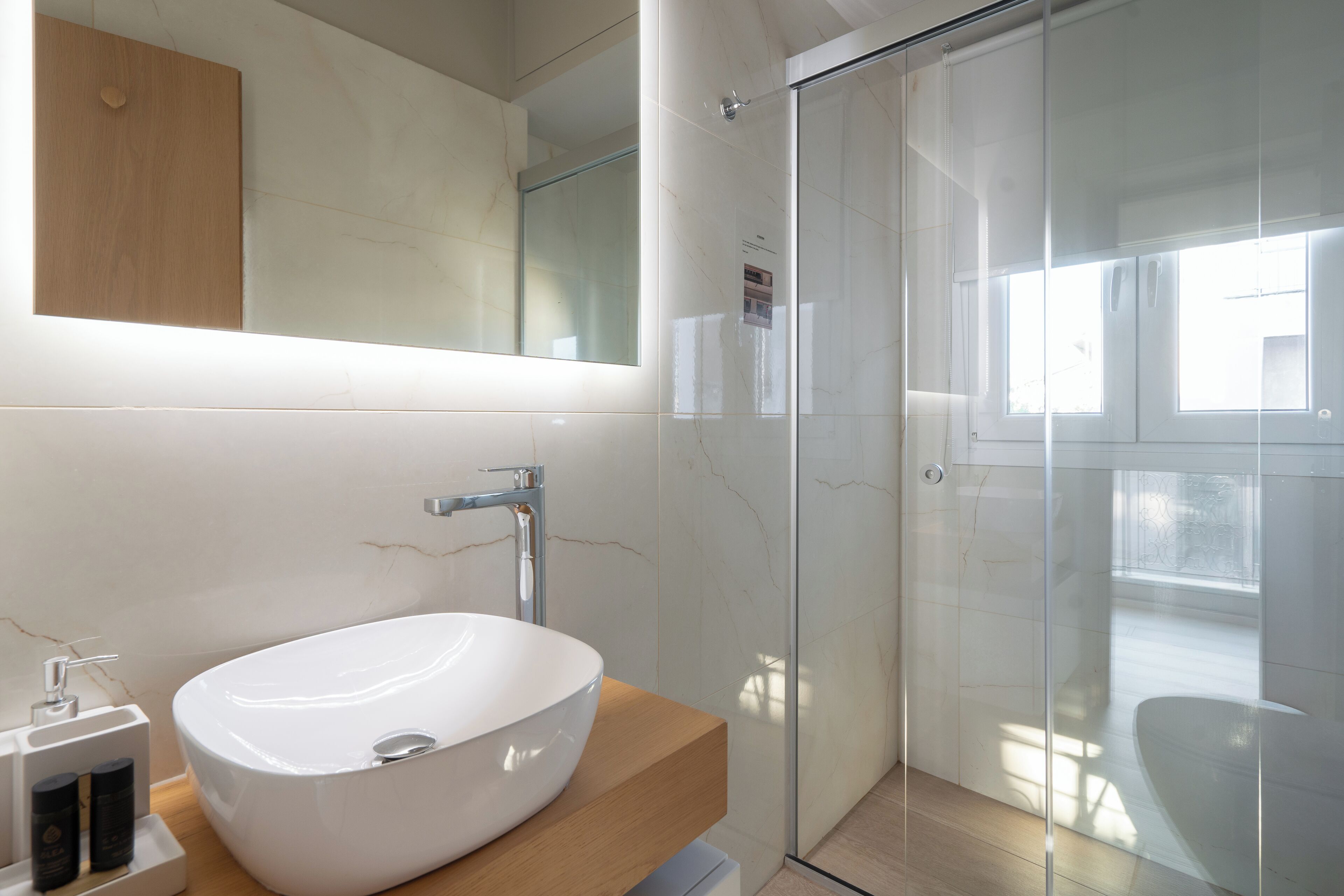 A modern bathroom with a large oval sink, a wooden vanity, a glass shower enclosure, and a large mirror above the sink.
