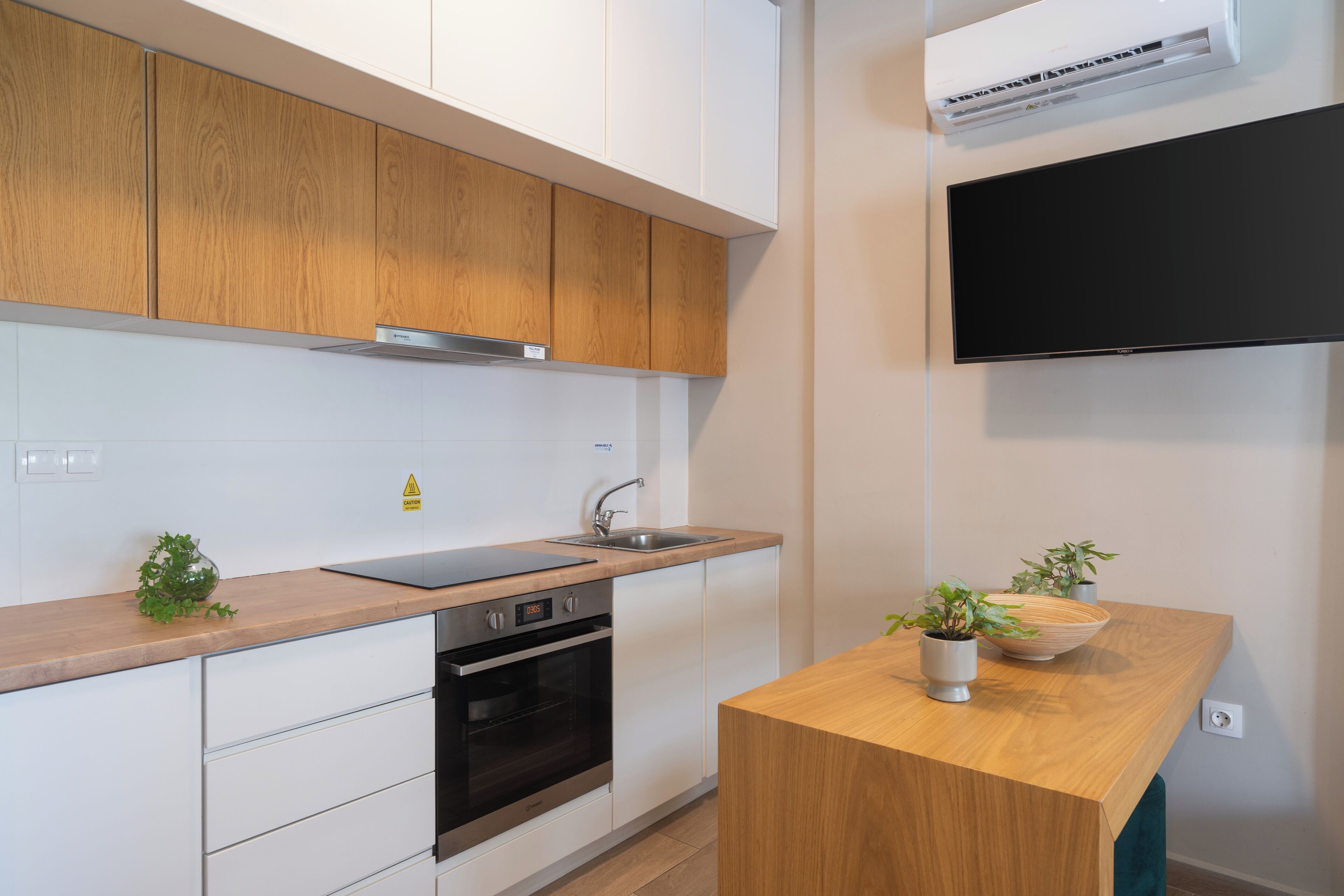 Une cuisine moderne avec des meubles en bois, un four encastré, un évier et un téléviseur à écran plat fixé au-dessus du plan de travail.