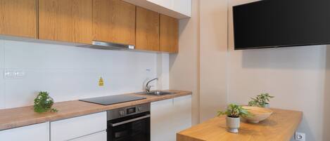 A modern kitchen with wooden cabinets, a built-in oven, a sink, and a flat-screen TV mounted above the counter.