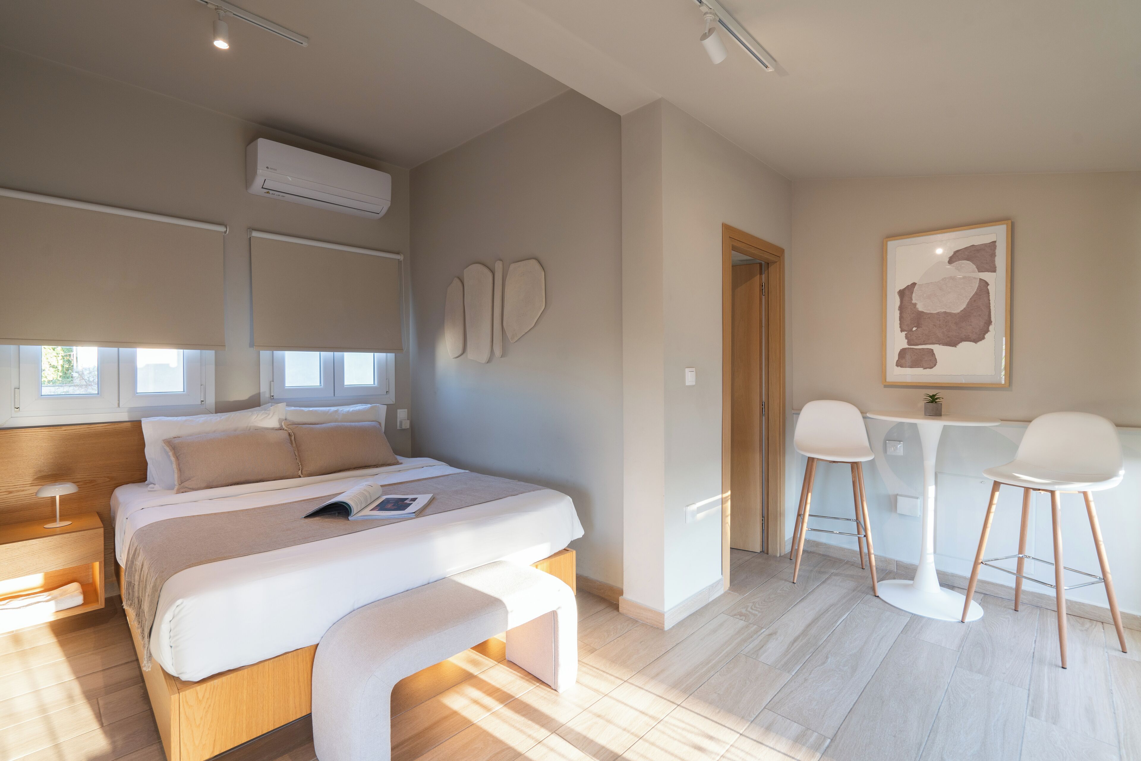 Een moderne slaapkamer met een groot bed, nachtkastjes, een bureau met twee stoelen en een wandairconditioner.