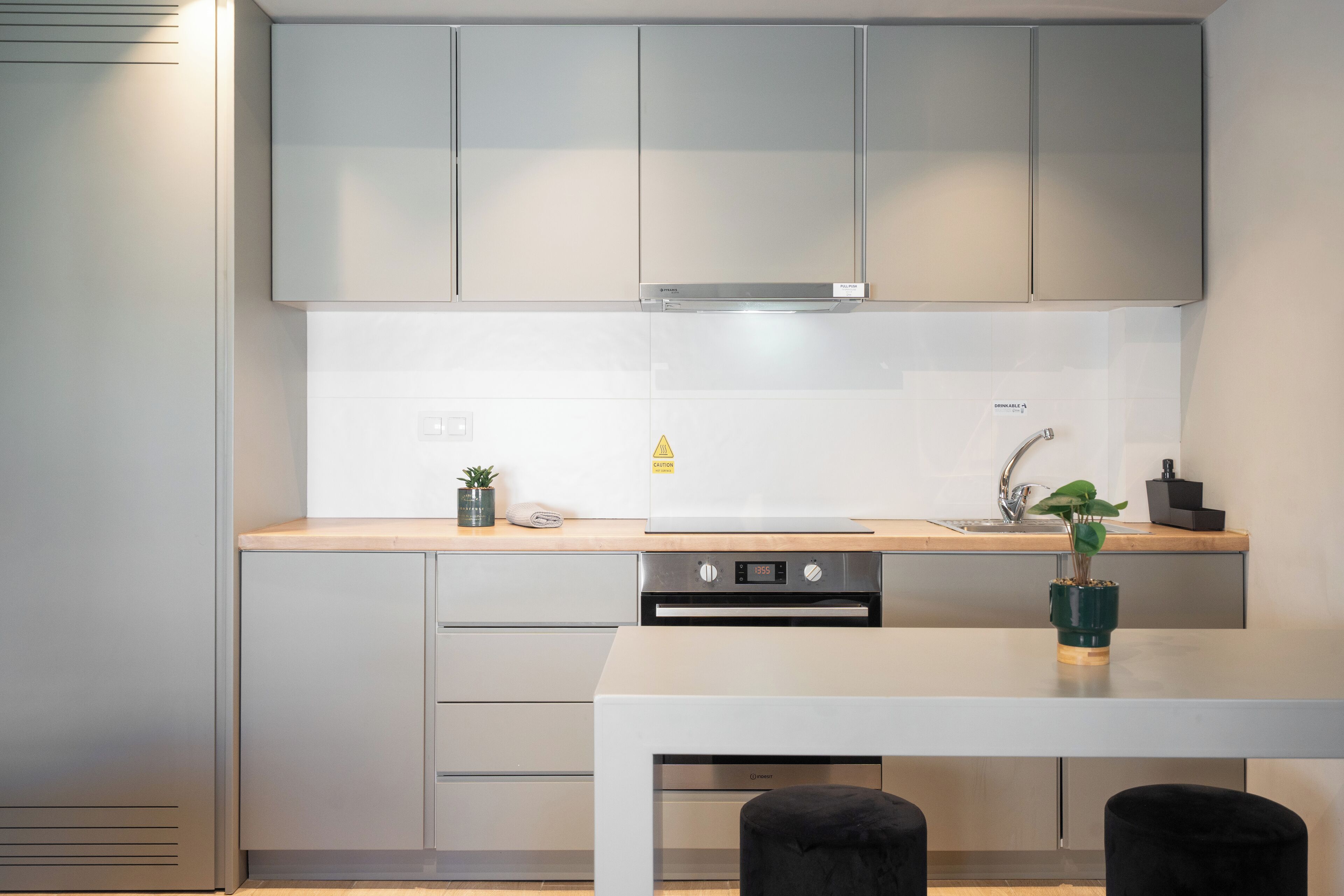 A modern kitchen with grey cabinets, a stainless steel range hood, a built-in oven, and a sink with a faucet.
