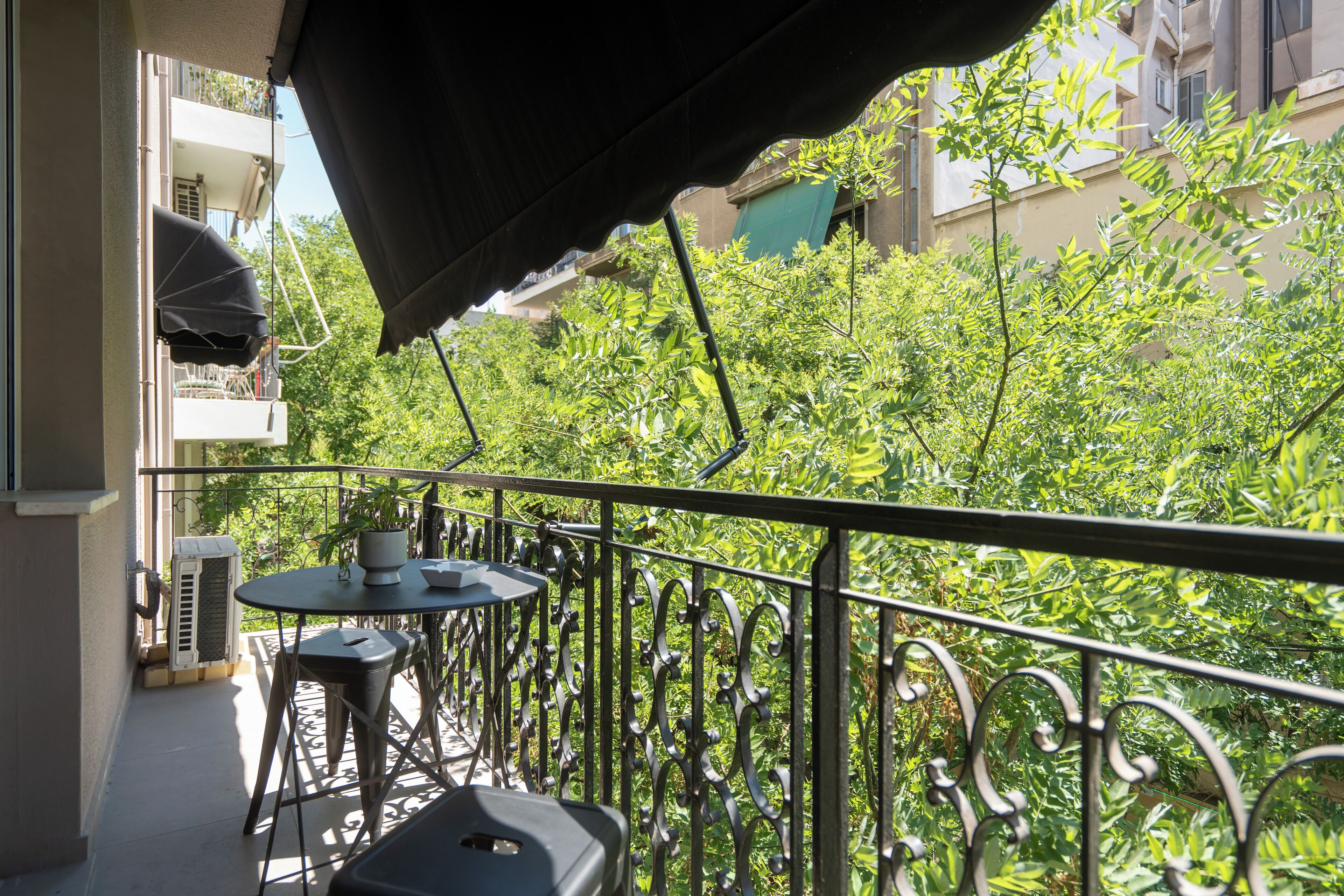 Un balcon avec une table et des chaises, un pot de fleurs et une vue sur la verdure et les bâtiments.