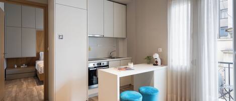 A compact kitchen with a central island, wooden flooring, and a view of the balcony through sheer curtains.