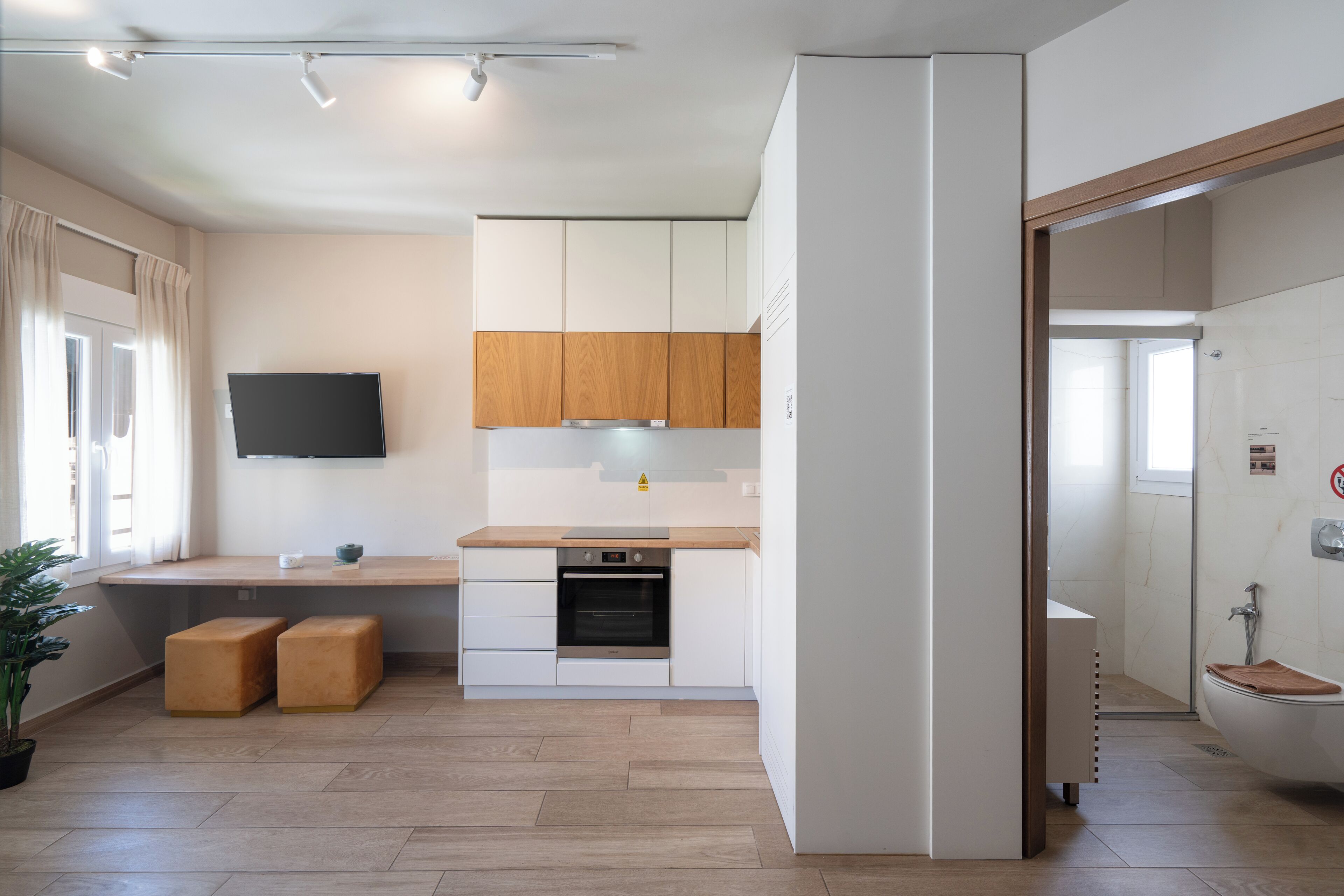 A modern kitchen with wooden cabinets, a built-in oven, and a flat-screen TV on the wall.
