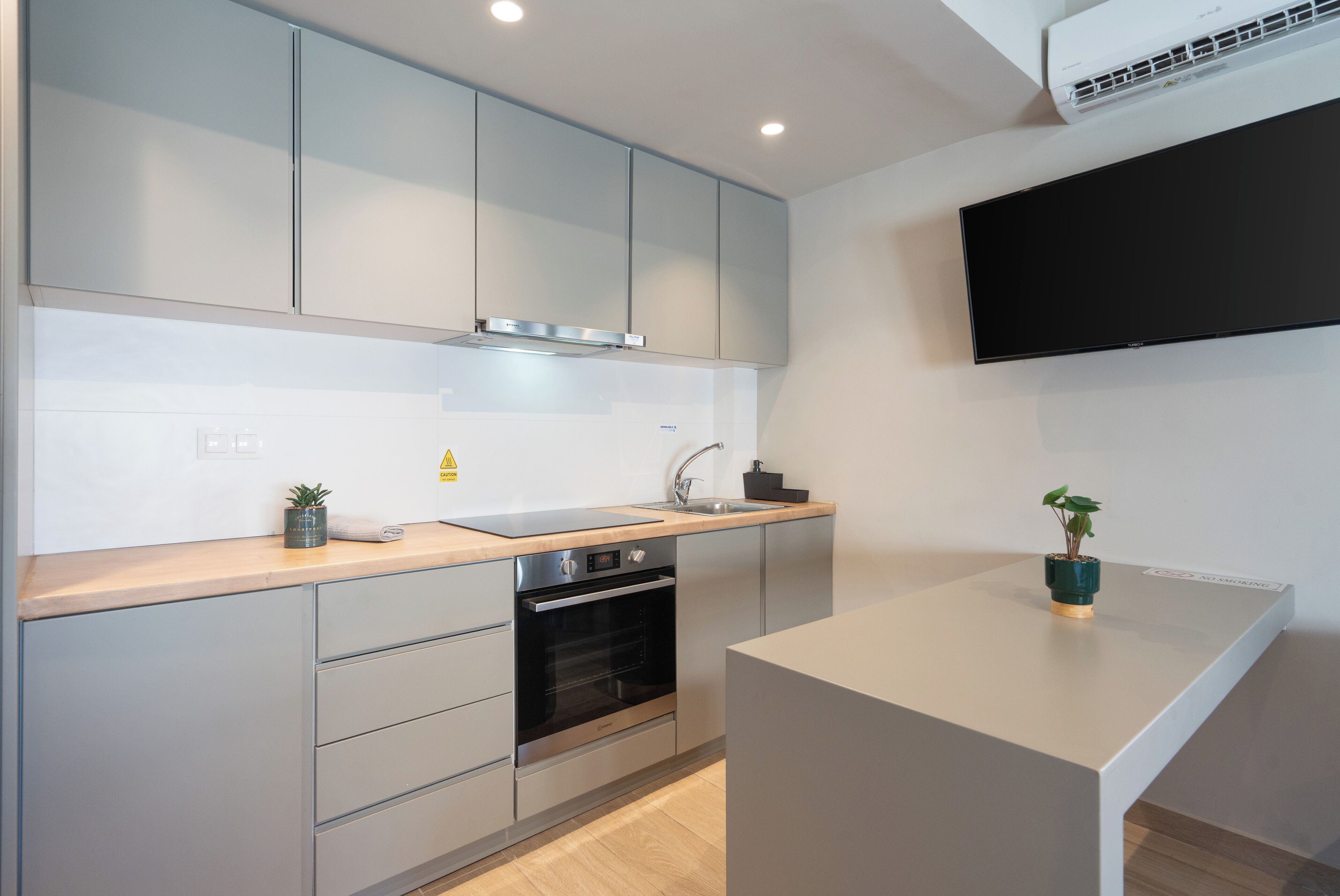 A modern kitchen with grey cabinets, a built-in oven, a sink, and a small island with a plant.