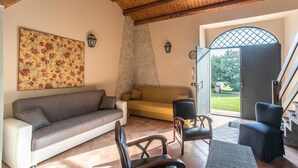 Un salon comprenant un canapé, des fauteuils et une porte donnant sur un espace extérieur avec vue sur la verdure.