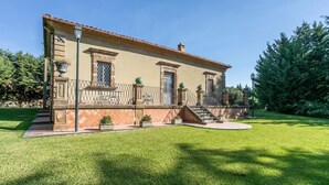 Un bâtiment à deux étages, doté d’un toit en tuiles, d’une façade en pierre et d’un petit jardin avec une pelouse et des plantes en pot.