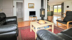 Un salon avec des canapés en cuir, un téléviseur, une table en bois, une cheminée et une vue sur l’extérieur, visible à travers une porte vitrée.