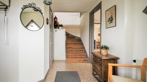 Un couloir avec un escalier en bois, un miroir, une commode et une porte donnant sur une pièce.