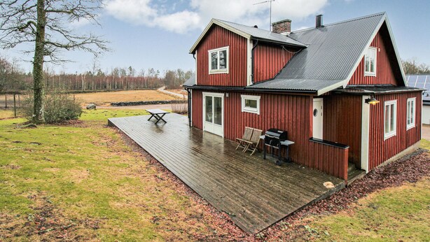 Une maison en bois rouge avec une terrasse, une table et une chaise.