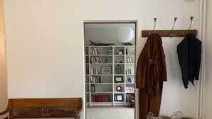 A room with a wooden bench, a bookshelf filled with books and decorative items, a coat rack with jackets, and woven baskets on a small table. - Family home, its park and streams, on the route des Châteaux (Huisseau-sur-Mauves)