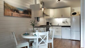 A modern kitchen with white cabinetry, a dining table set for two, and a painting of a beach scene on the wall. - Nice home in Heinkenszand with sauna (Heinkenszand)