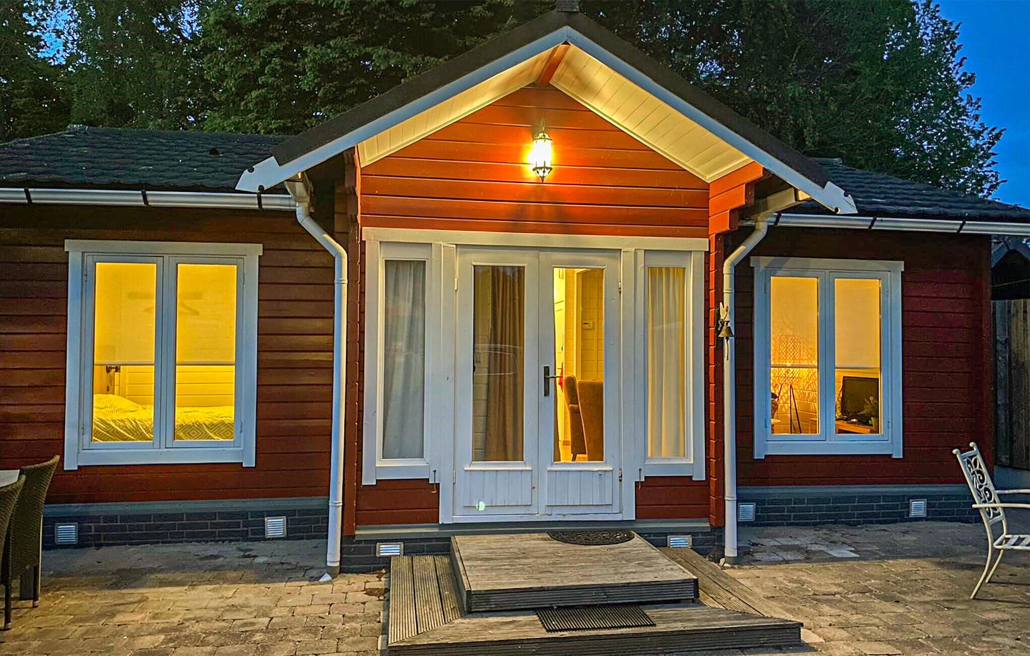 Une cabane en bois avec deux grandes fenêtres, un porche à l’avant et un luminaire au-dessus de l’entrée.