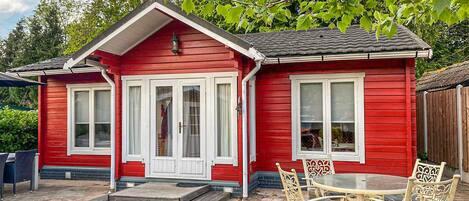 A red wooden house with a front porch, two windows, and a small table with chairs.