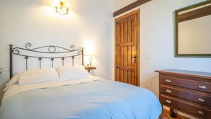 Ein Bett mit Kopfteil, eine Nachttischlampe, ein Holzschrank und ein Spiegel an der Wand.