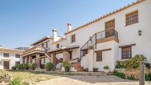 Ein traditionelles Gebäude im mediterranen Stil mit Innenhof, einem zentralen Treppengehäuse, zahlreichen Fenstern und Blumentöpfen.