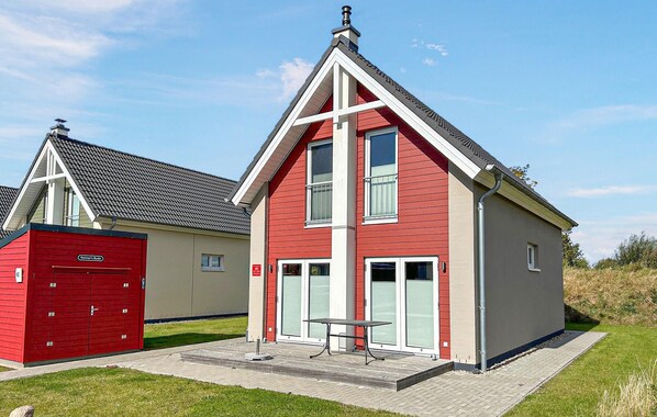 Un bâtiment rouge et beige avec un toit triangulaire, un garage rouge et une terrasse dallée avec une table et des chaises.