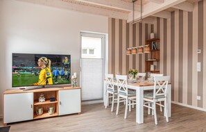 Un salon moderne avec un téléviseur, une table à manger en bois, des chaises blanches et un papier peint à rayures.