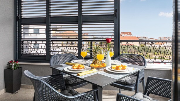 A balcony with a table set for breakfast, featuring orange juice, pineapple, and a red rose.