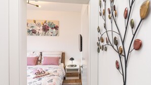 A bedroom with a bed, pillows, a bedside table with a lamp, a wall-mounted light fixture, and a decorative wall piece.