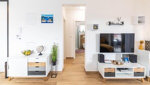 A modern living room with a white TV stand, a flat-screen TV, and a white cabinet with drawers.