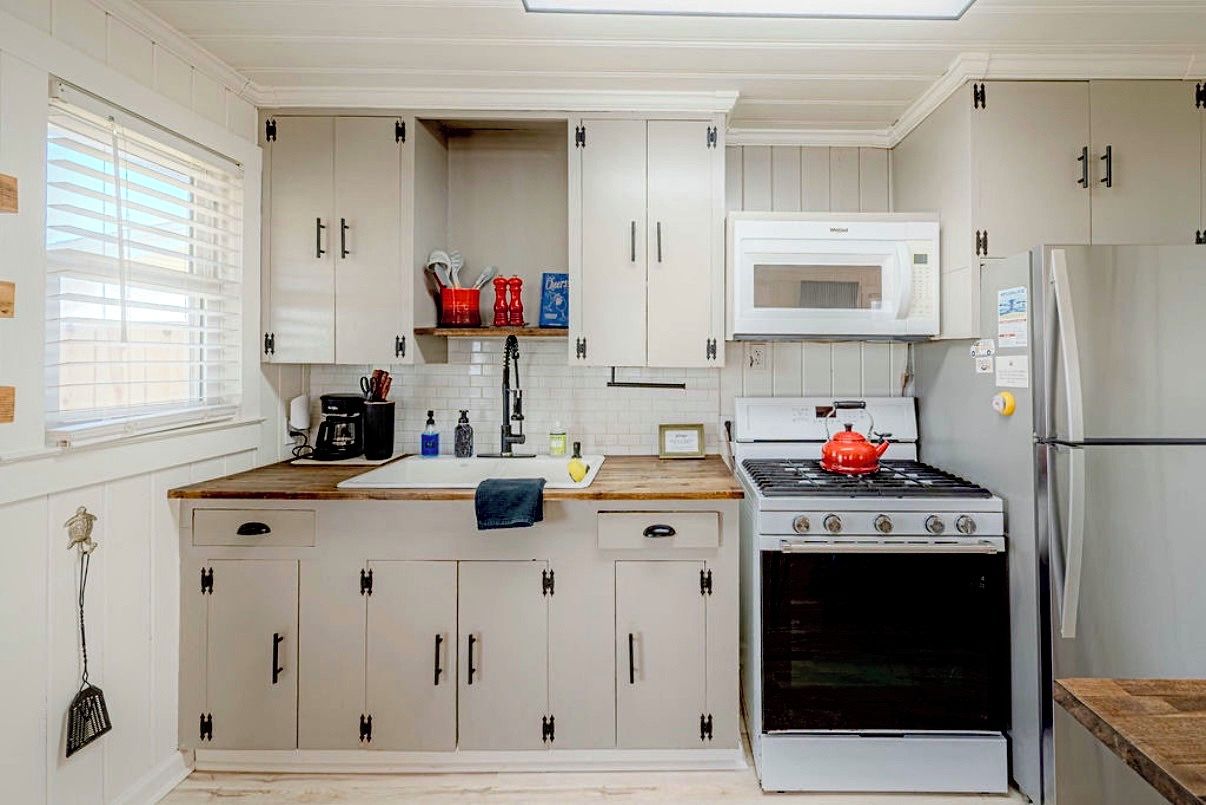 Una cocina con armarios blancos, microondas, estufa y refrigerador.
