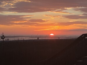A sunset over the ocean with silhouettes of people and a beach fence.