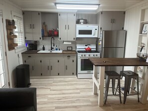 A modern kitchen with white cabinets, a stainless steel refrigerator, a microwave, a stove, and a sink.
