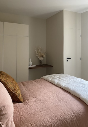 Een slaapkamer met een bed, een kledingkast, een plank met decoratieve objecten en een deur.