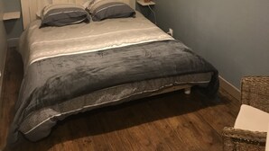 A bedroom with a wooden headboard, a bed with grey bedding, a nightstand with a lamp, and a wall-mounted dreamcatcher.