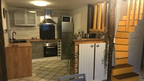A compact kitchen with a sink, stove, oven, microwave, and refrigerator. There is a dining table with chairs and a staircase leading to an upper level.