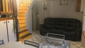 A living room with a black leather sofa, a staircase with wooden steps, and a tiled floor.