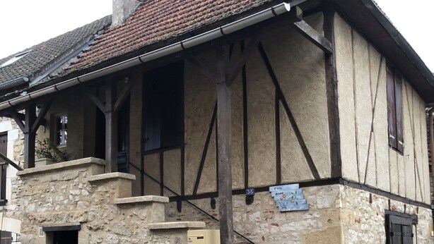 A traditional half-timbered house with a stone base, a tiled roof, and a small front porch.