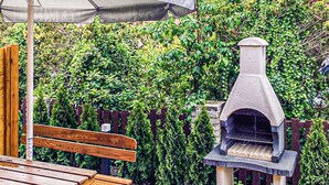 Una panchina in legno e un barbecue in pietra in un giardino con recinzione in legno e vegetazione rigogliosa.