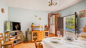A dining area with a table set for four, a television on a wooden stand, and a view of a swimming pool through an open door. - Nice home in Cortegana (Cortegana)