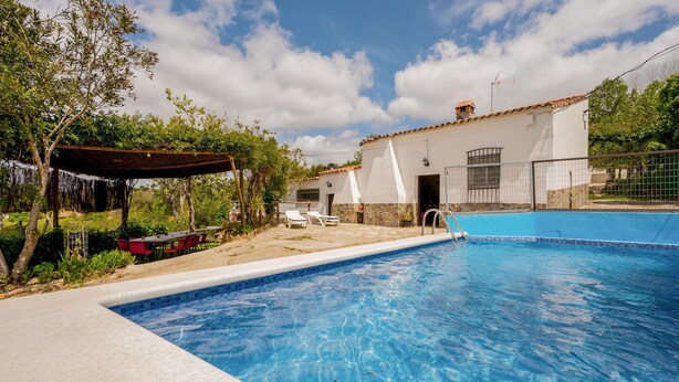 A swimming pool with a clear blue water, surrounded by a patio area with outdoor seating and a covered section. - Nice home in Cortegana (Cortegana)