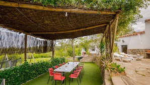 An outdoor patio with a table and chairs, surrounded by greenery and a pergola structure. - Nice home in Cortegana (Cortegana)