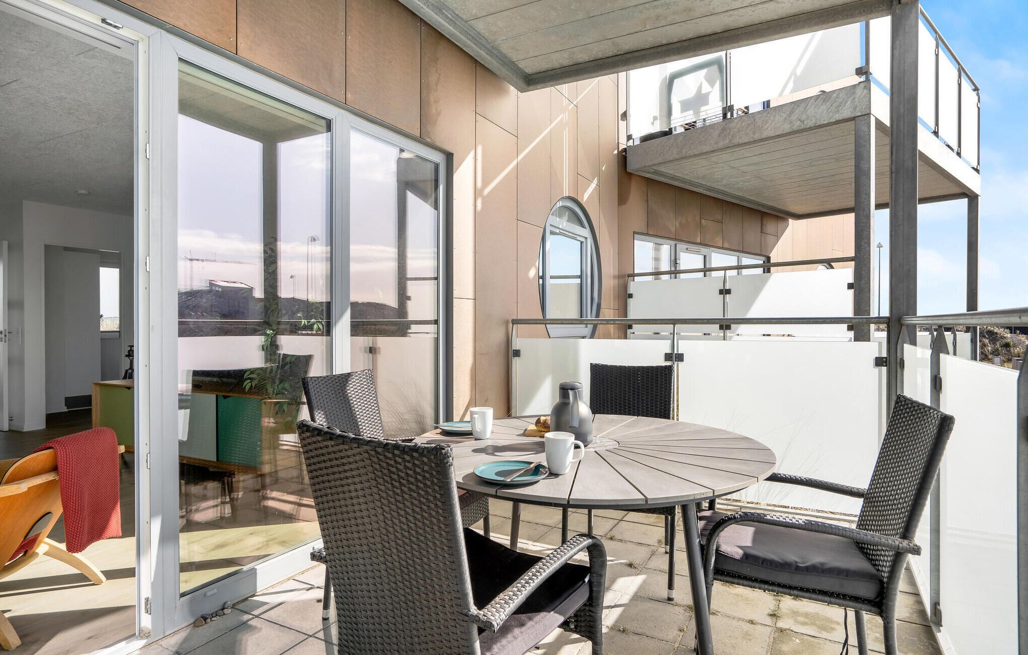 Een balkon met een ronde tafel en rieten stoelen, een schuifdeur en uitzicht op de stad.
