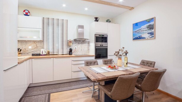 A modern kitchen with white cabinets, a wooden countertop, and a dining area with a wooden table and four chairs. - Nice apartment in Sinj with WiFi (Sinj)