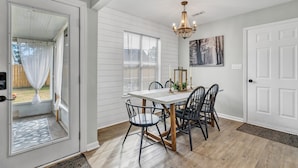 A dining area with a white table, black chairs, a chandelier, and a view through a glass door to the outside. - Pet Friendly Fenced Backyard Game Room Patio Firepit Trailer Motorcycle Parking (Myrtle Beach)