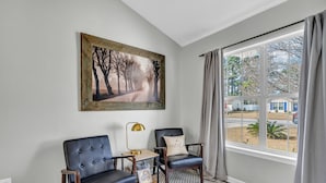 A room with two leather armchairs, a framed picture on the wall, a lamp, and a view of the outside through a large window. - Pet Friendly Fenced Backyard Game Room Patio Firepit Trailer Motorcycle Parking (Myrtle Beach)
