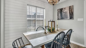 A dining area with a white table, black chairs, a chandelier, and a painting on the wall. - Pet Friendly Fenced Backyard Game Room Patio Firepit Trailer Motorcycle Parking (Myrtle Beach)