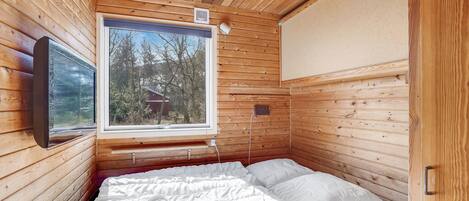 Ein Zimmer in einer Holzhütte mit Bett, Fenster und einem Wand-Fernseher.