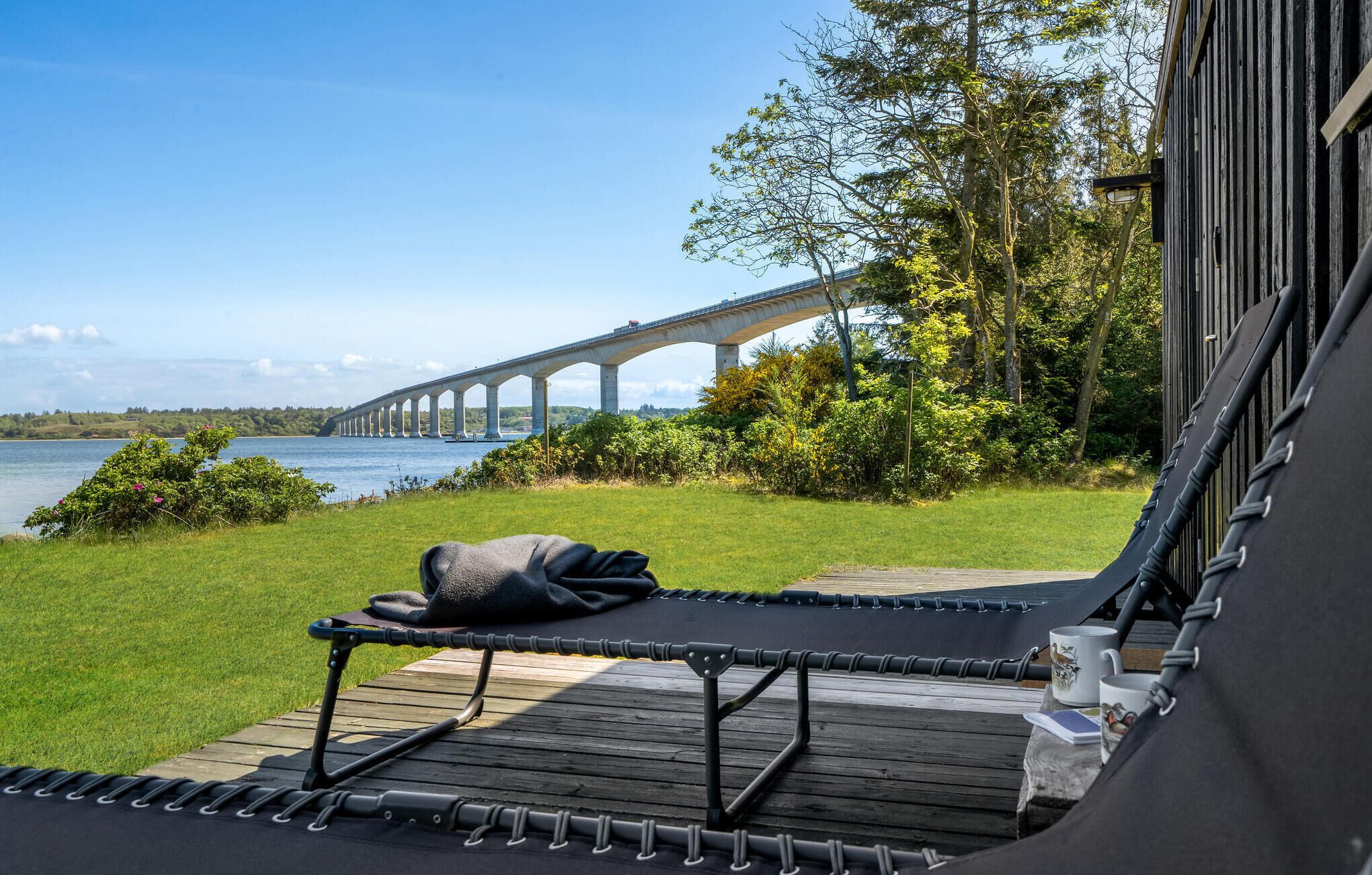 En træterrasse med hængekøje og udsigt til en bro over vand.