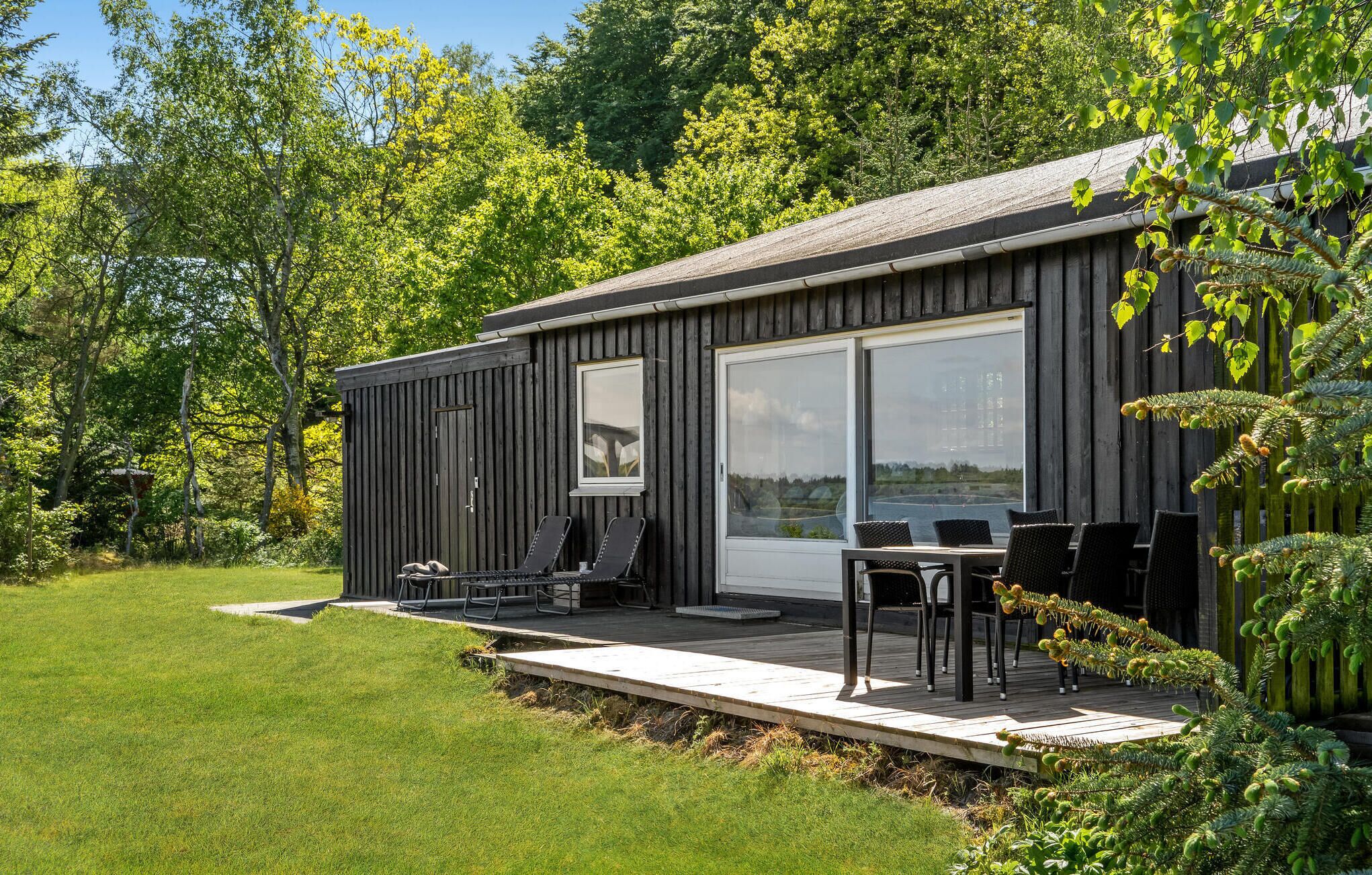 Una cabaña moderna con terraza, mobiliario exterior y ventanas amplias con vistas a un área boscosa.