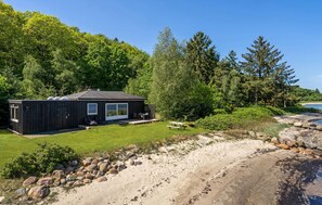 Une cabane dotée d’une terrasse, entourée d’une pelouse et d’arbres, située près d’une côte rocheuse.