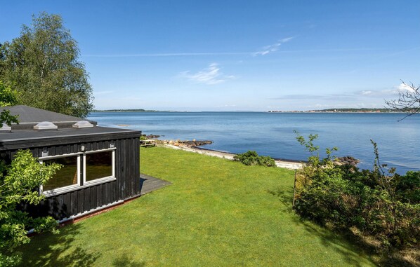 Une maison moderne dotée d’une grande fenêtre, d’une cour verdoyante et offrant une vue sur un lac paisible.