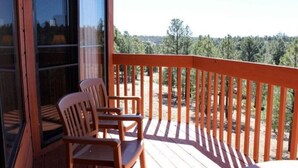 A wooden deck with a railing, two wooden chairs, and a view of a forested area. - Price REDUCED  2Bed 2Bath, Full Kitchen & dining area, Washer/Dryer. Golf nearby (Flagstaff)