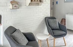 Una habitación con pared de ladrillo blanco, dos sillones grises con cojines, una mesita pequeña y suelo de madera.